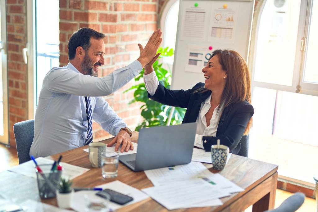 Two business people doing high five over table with laptop and papers. Image from Unsplash-krakenimages