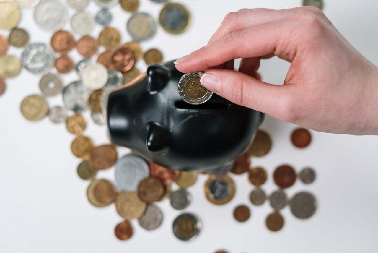 person putting coins into piggy bank with coins on table