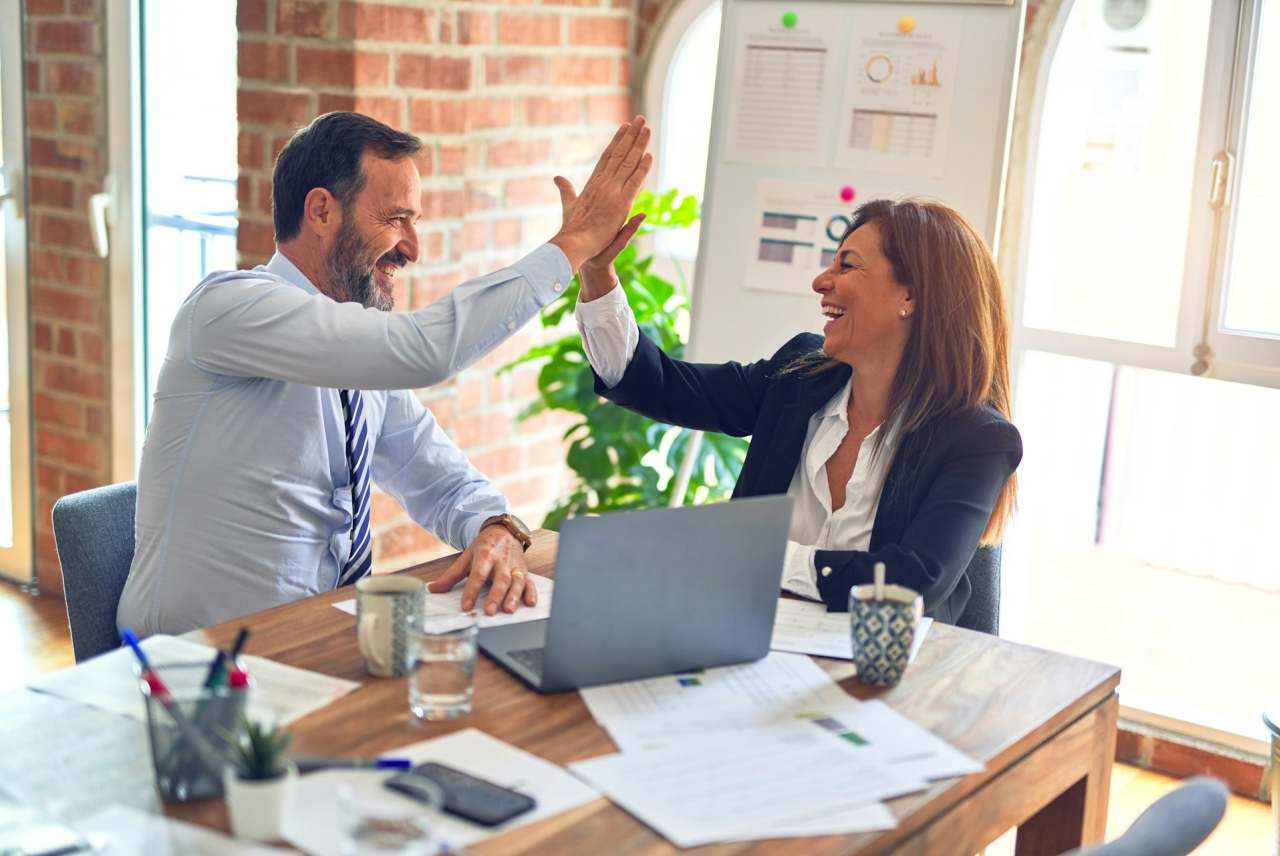 Two business people doing high five over table with laptop and papers. Image from Unsplash-krakenimages